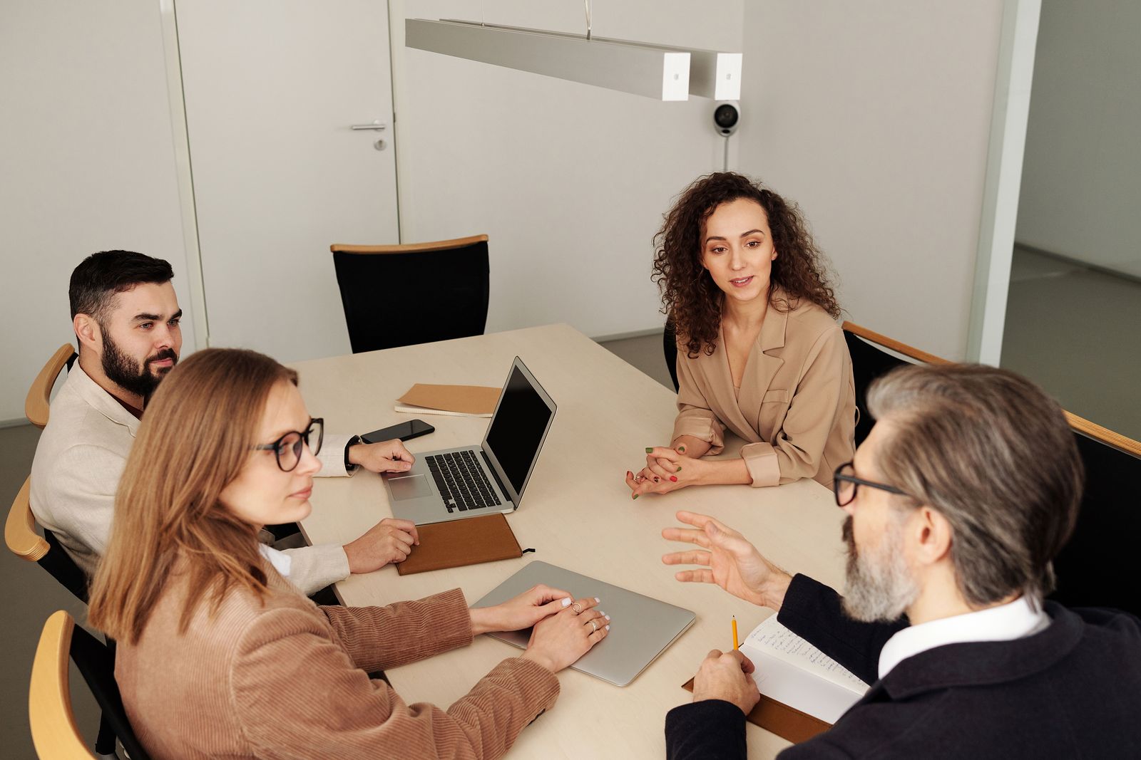 A group of colleagues in conversation around a bright office table with a laptop and notebooks.