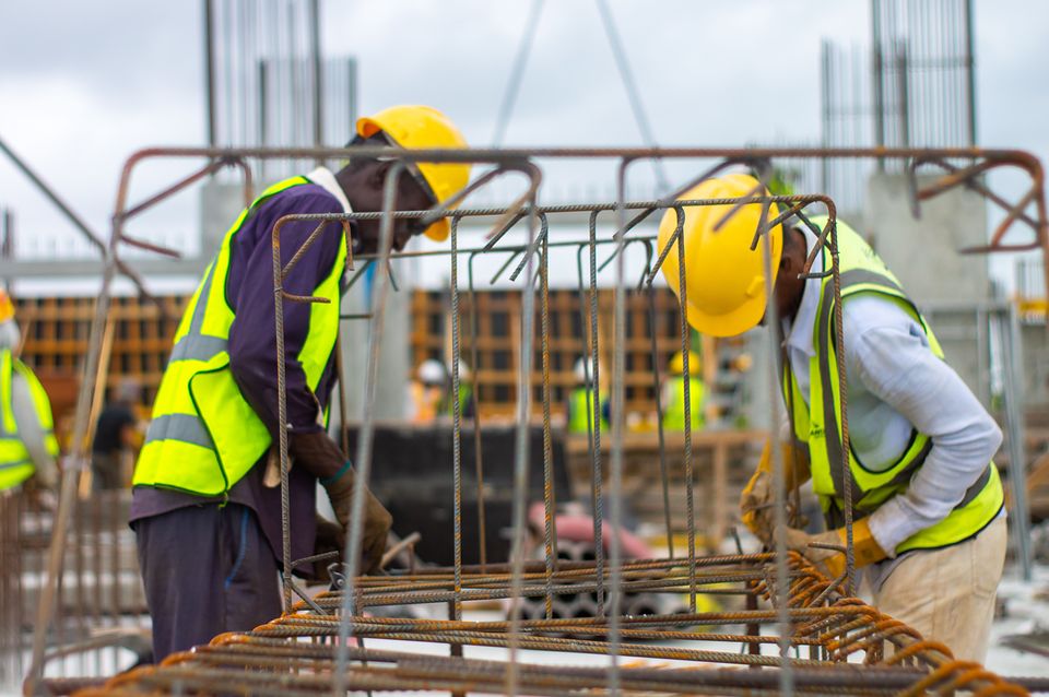 Two construction workers in hard hats tying rebar on a building site.