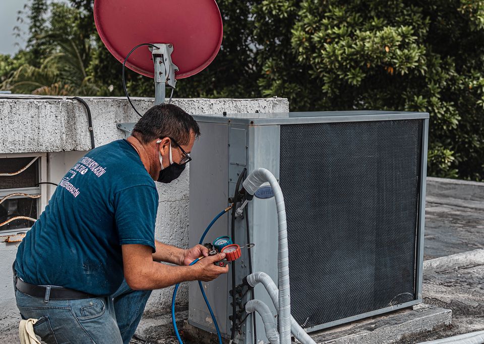 A technician checking a rooftop air conditioning unit with gauges.