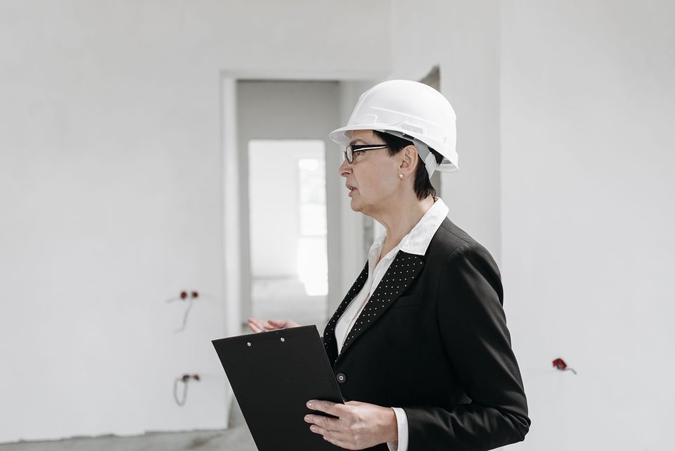 An inspector in a white hard hat reviews a clipboard inside a building under construction.