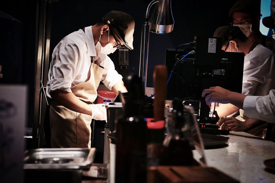 Cooks in white jackets and caps preparing food in a commercial kitchen.