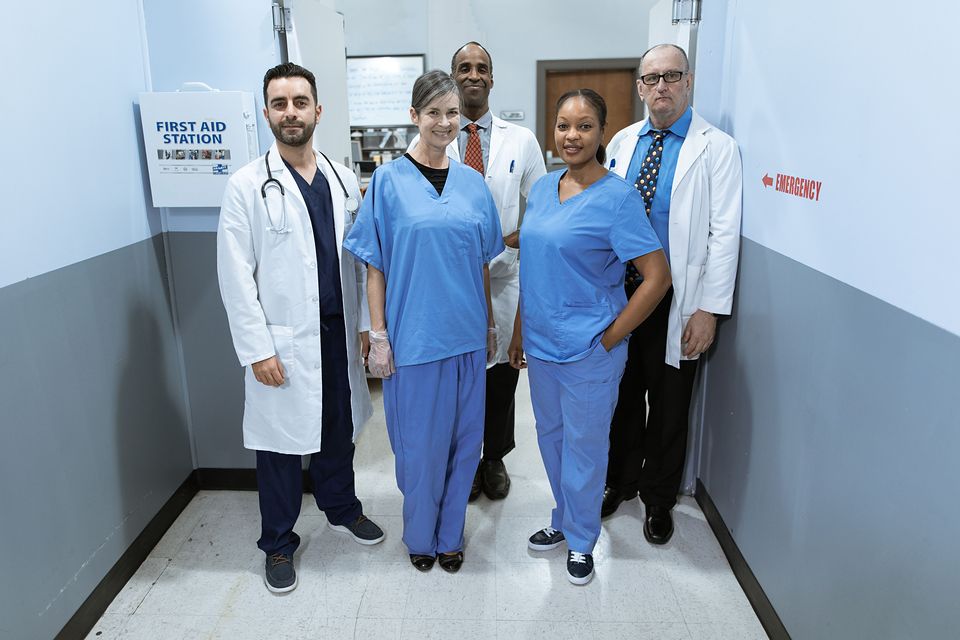 A team of five doctors and nurses standing together in a clinic hallway.