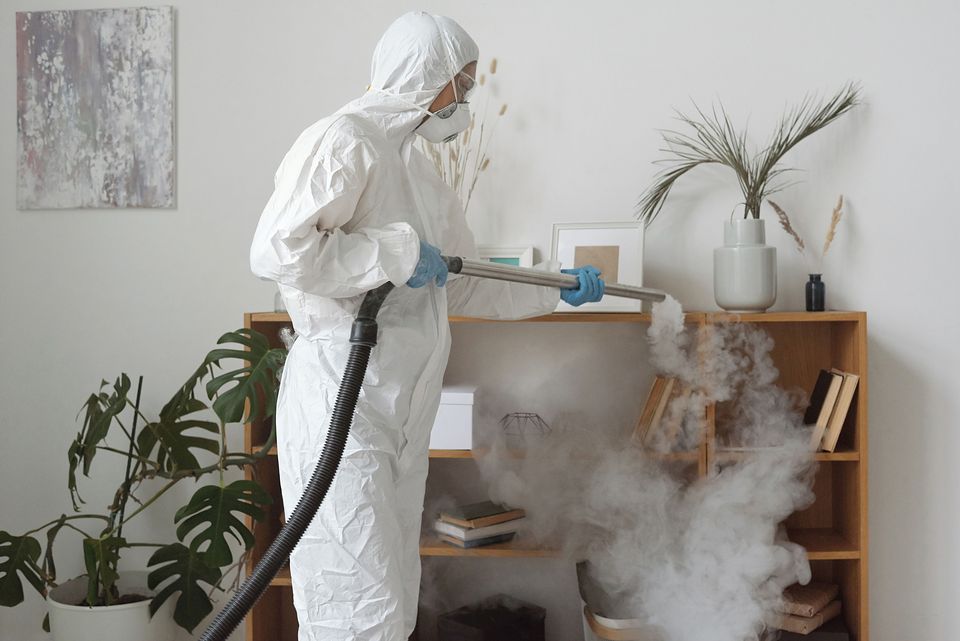 A technician in a white protective suit fogging a room for pest control.