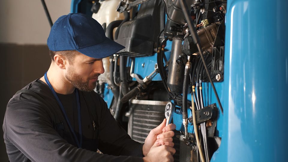 A mechanic in a cap tightening a fitting on a large machine.