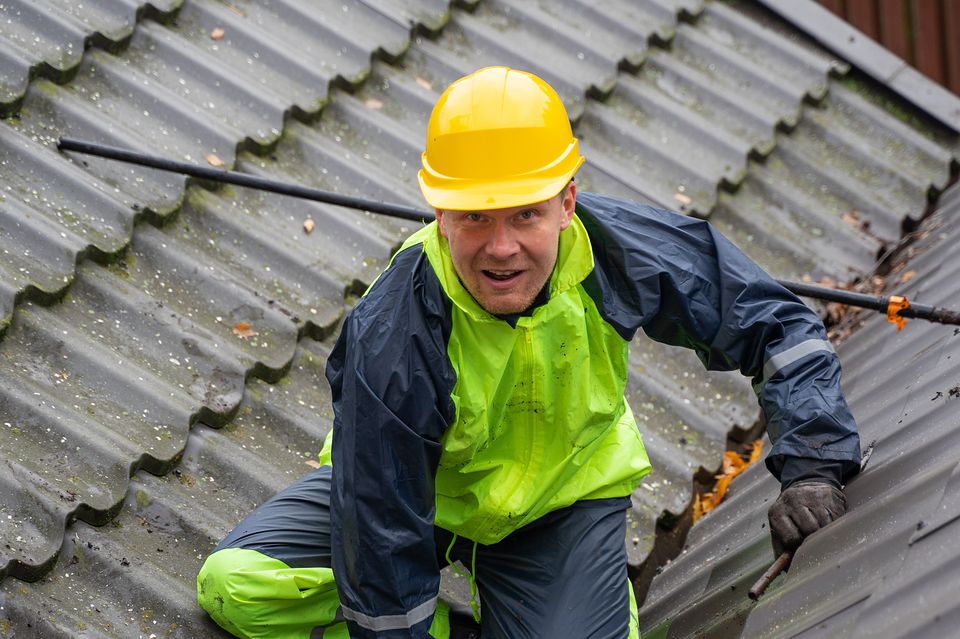 A roofer in a hard hat and safety vest working on a metal roof.