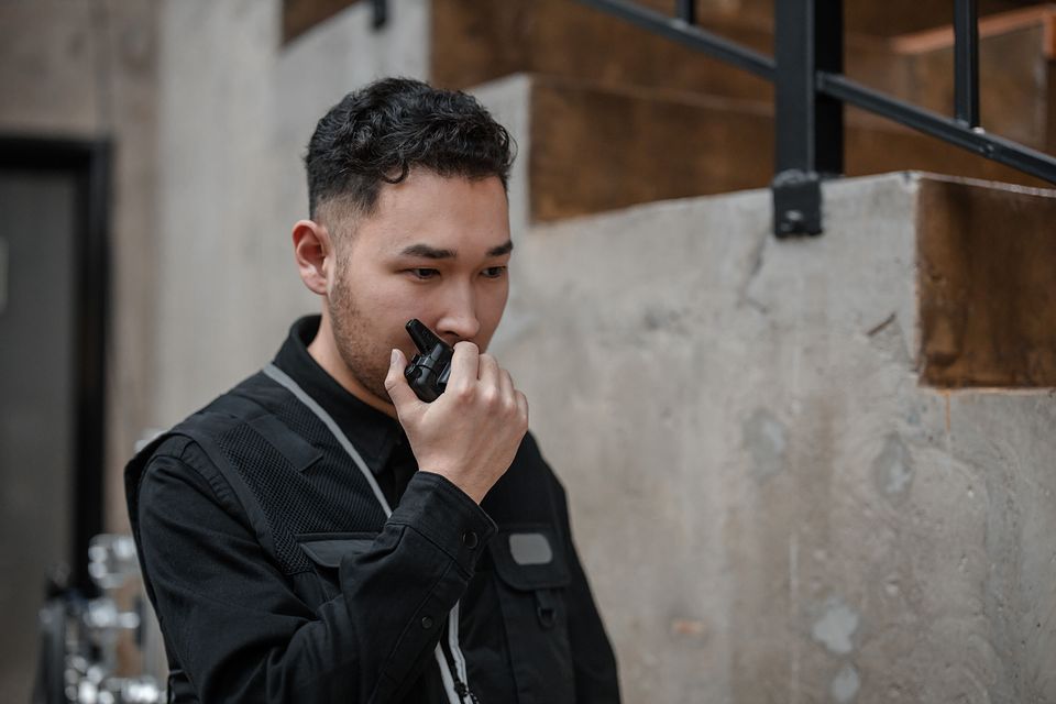 A security guard in a black uniform talking on a radio.