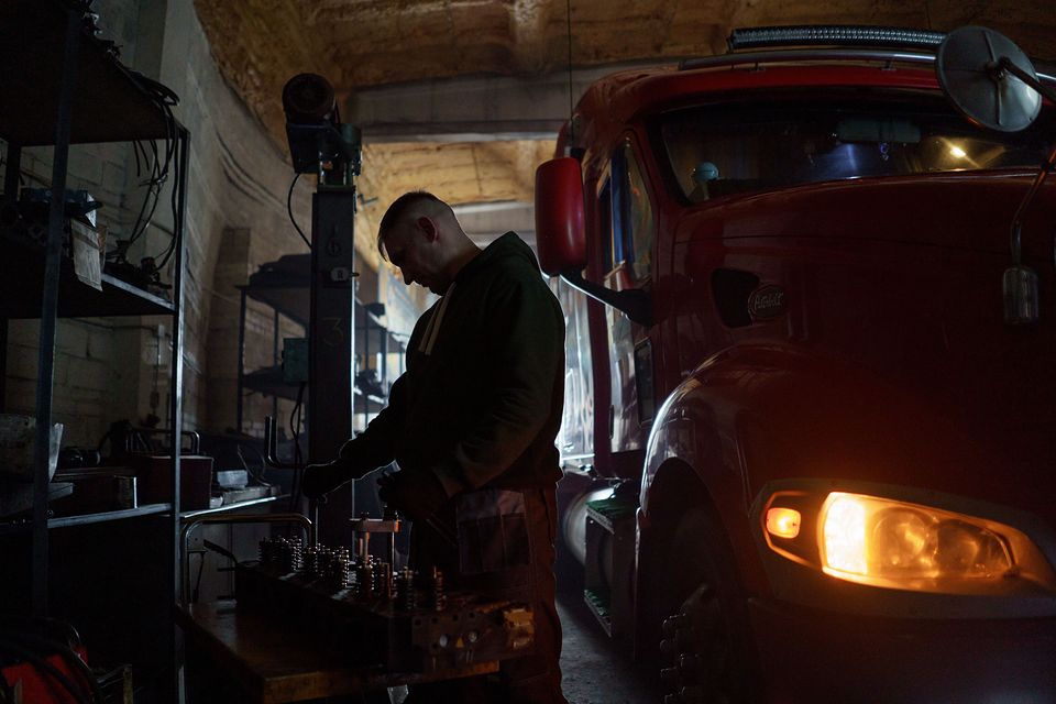 A mechanic working beside a red truck in a vehicle shop.