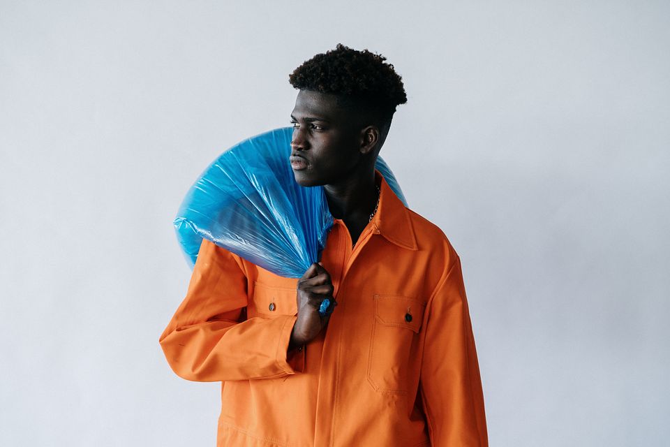 A sanitation worker in an orange uniform carrying a full trash bag.